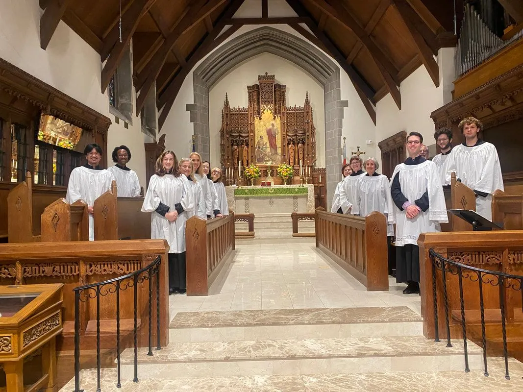 The St. James Choir in white surplices in the chancel, in front of the carved reredos