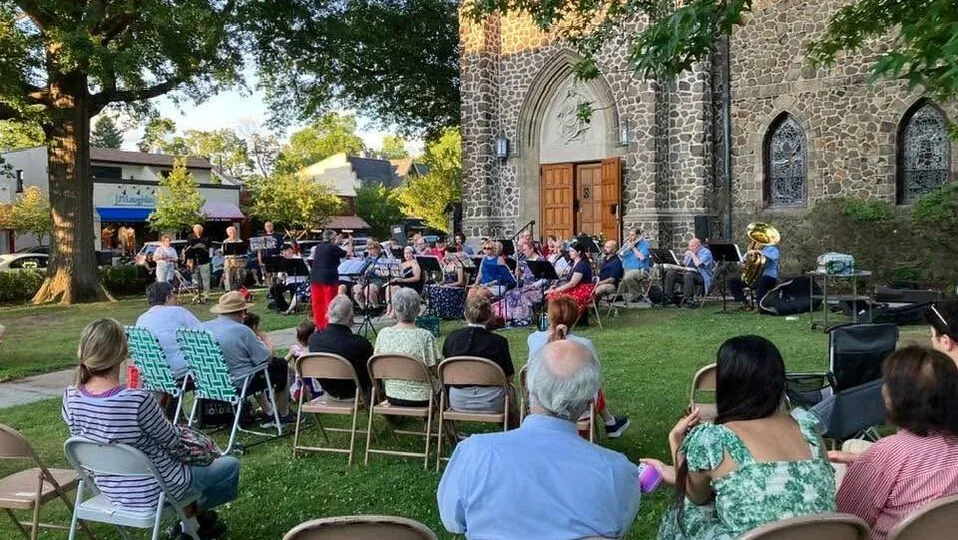 Neighbors in folding chairs listen to a band on the front lawn of St. James